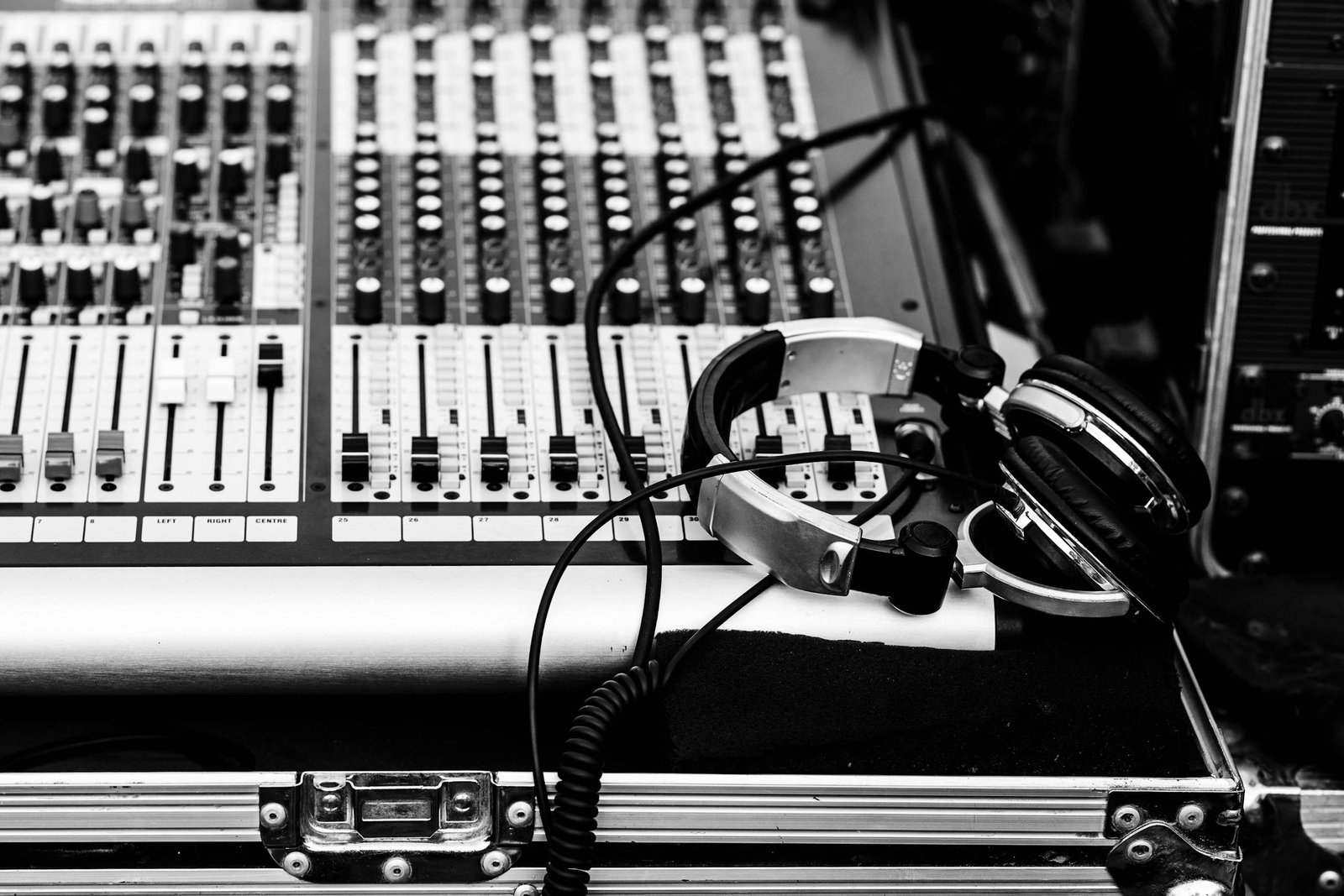 A detailed monochrome view of an audio mixer and headphones in a studio setting.